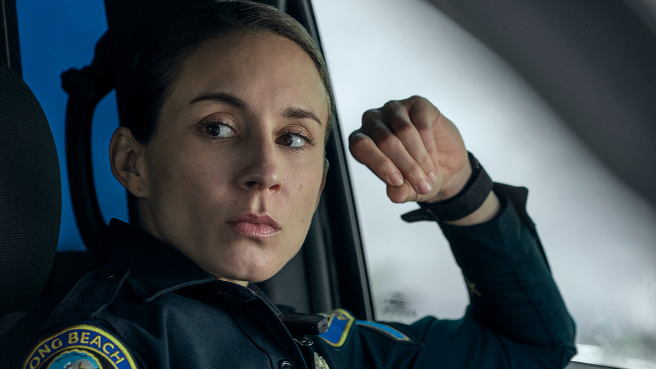 A woman with a police uniform sits in a car with a serious aspect of guard.