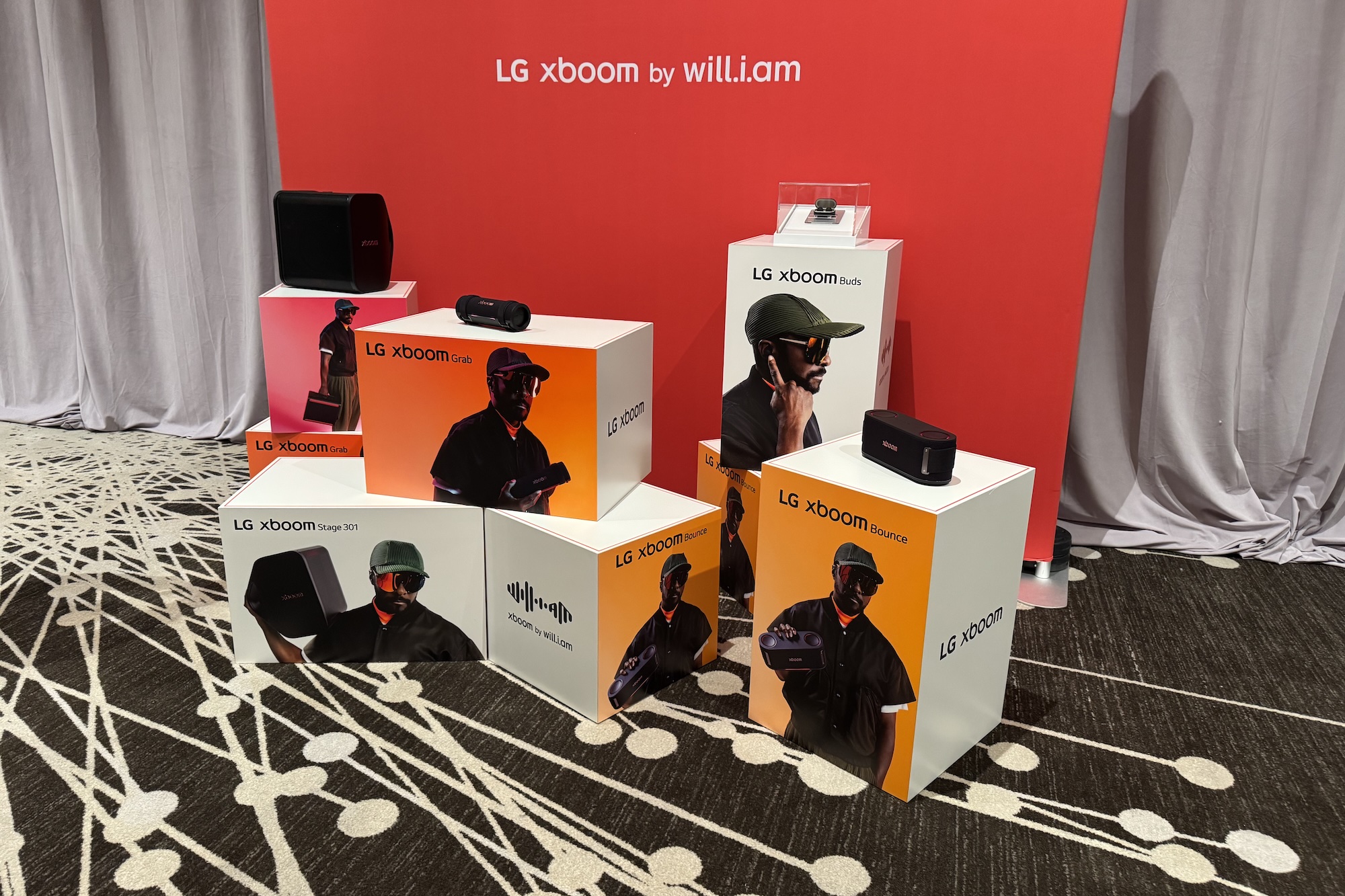 The line of xboom by will.i.am LG audio products on stands with a red background.