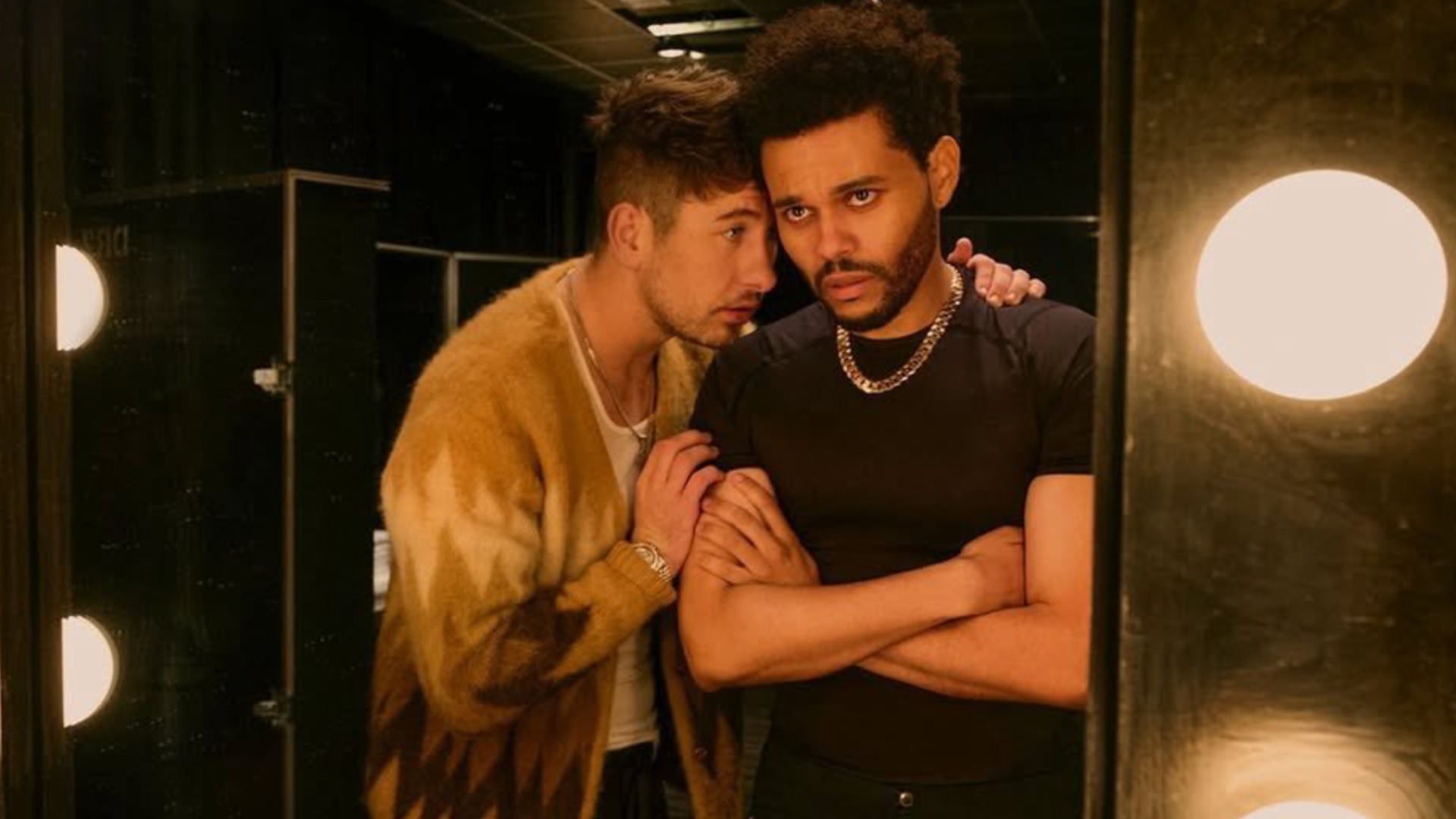 Barry Keoghan spricht The Weeknd ins Ohr, während sie in einen Spiegel starren.