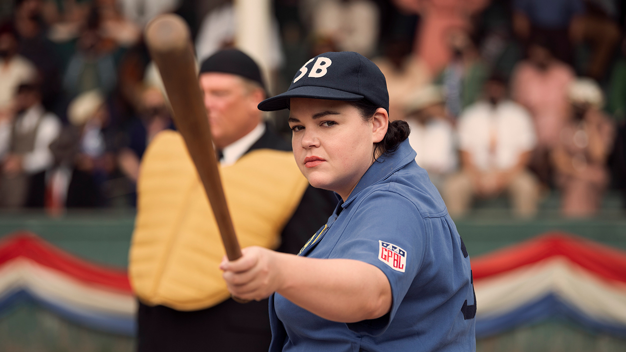 A woman in uniform at a baseball game pointing her bat to the outfield in A League of Their Own.