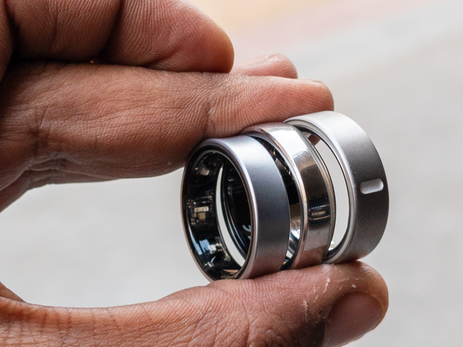 Oura Ring 4, Galaxy Ring und RingConn Gen 2 zwischen zwei Fingern gehalten