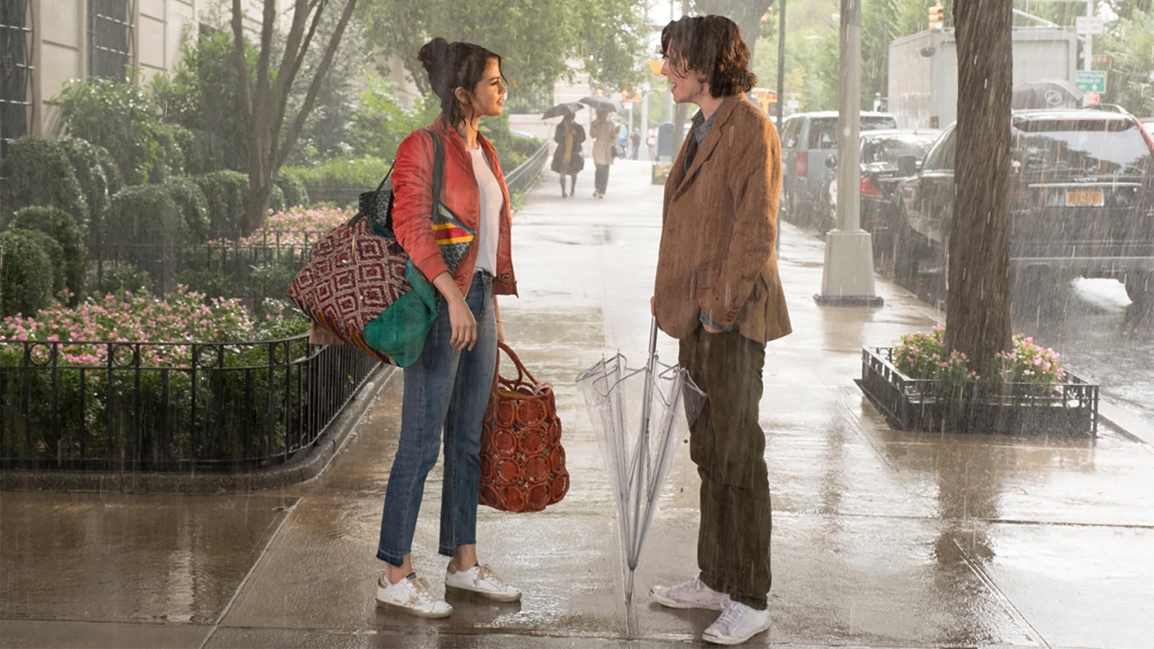 Uma mulher e um homem param para conversar na rua, debaixo de chuva, em Um dia chuvoso em Nova York.